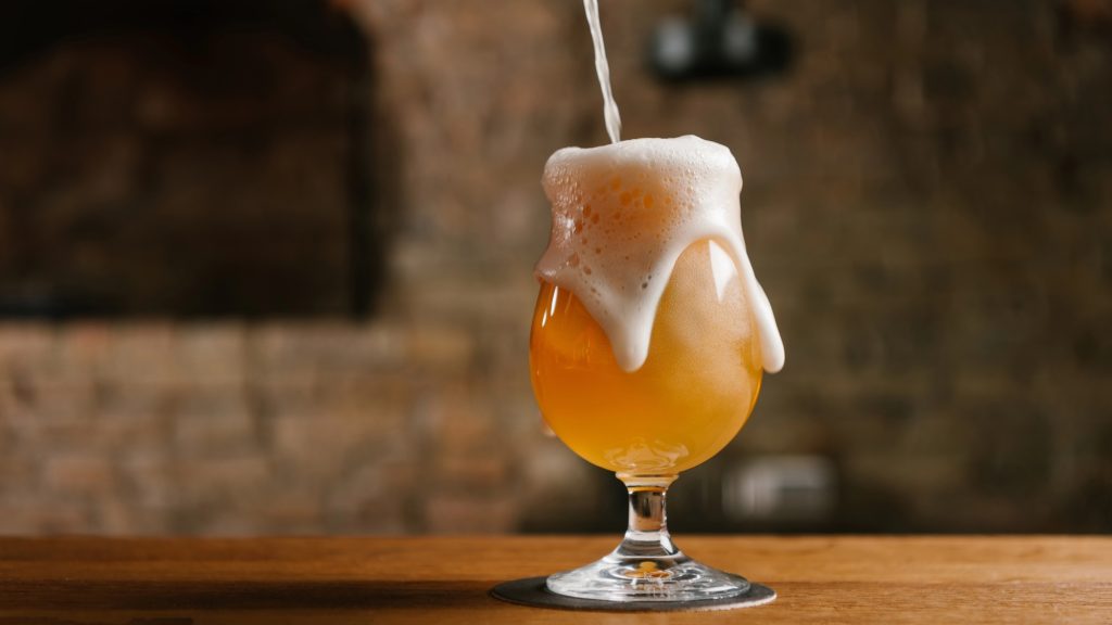 Stream of beer filling up glass with foam coming over sides