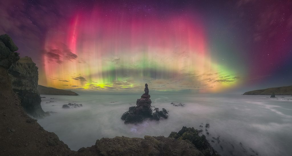 a pink, green, yellow aurora over mountain and clouds