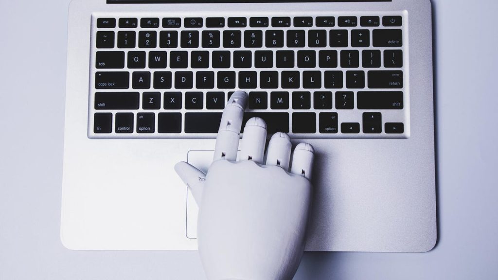 A robot hand presses a button on a laptop.