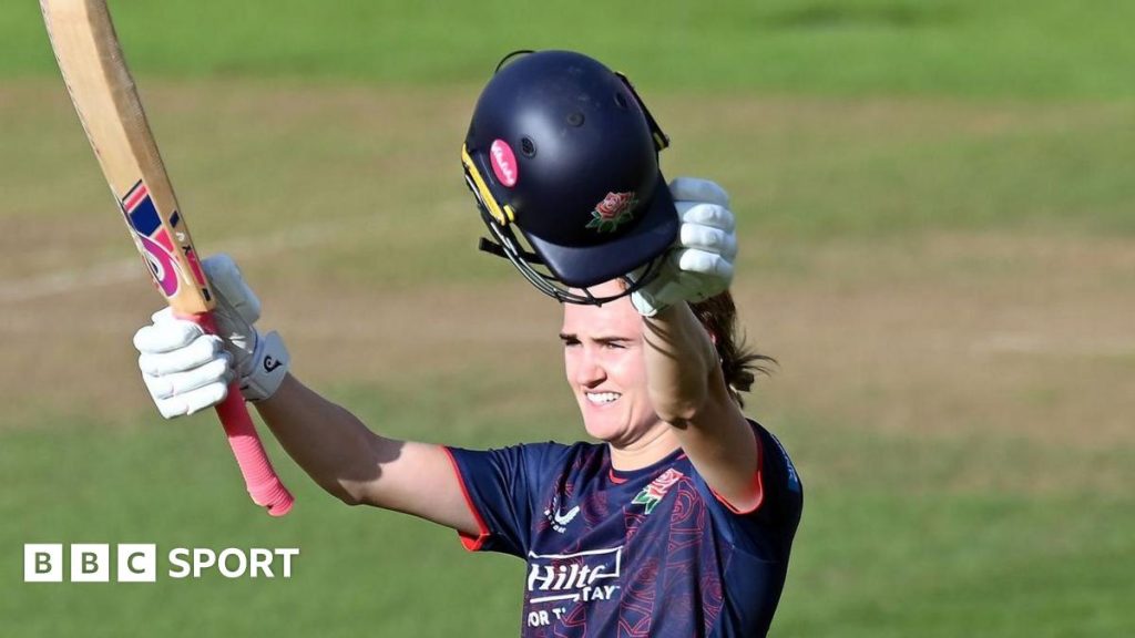 Lancashire batter Gaby Lewis raises her bat in one hand and helmet in the other to score a century