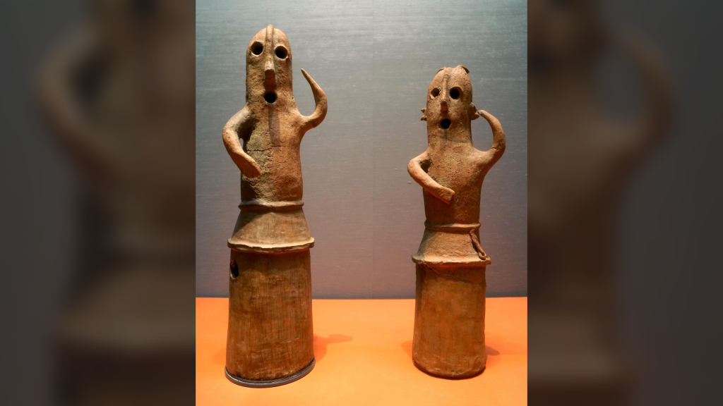 two cylindrical human-like terracotta figurines against a grey background